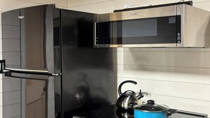 Una cocina compacta con un refrigerador negro, un microondas, una estufa y una tetera.