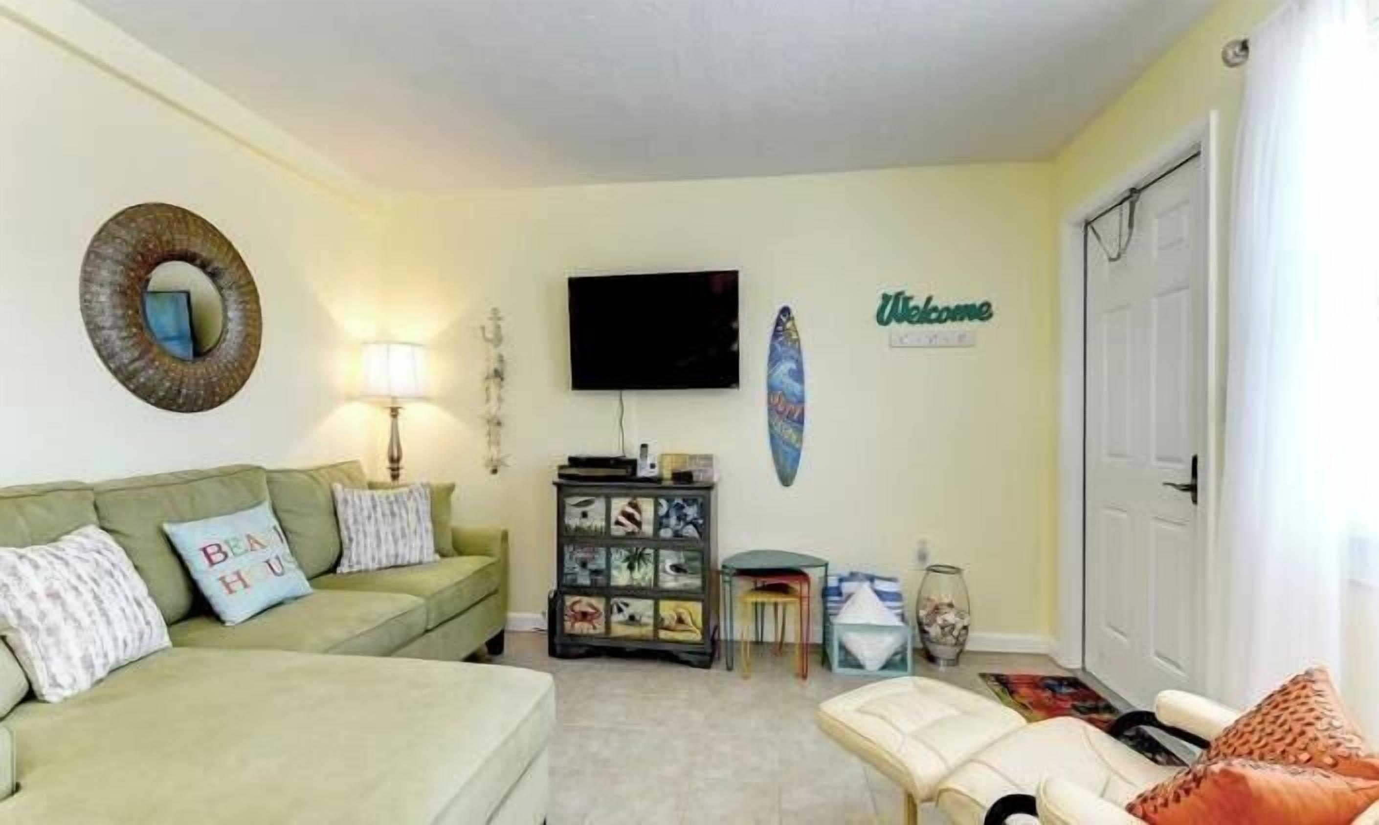 Una sala de estar con un sofá verde, una mesita, un televisor y una decoración con una tabla de surf.