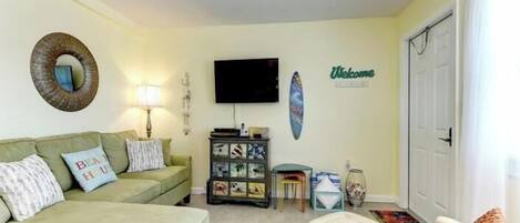Una sala de estar con un sofá verde, una mesita, un televisor y una decoración con una tabla de surf.