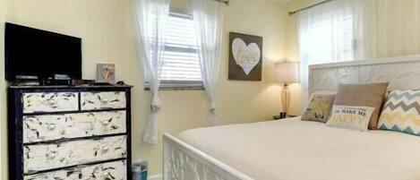 Une chambre à coucher avec un lit, un ventilateur de plafond, une télévision et une commode.
