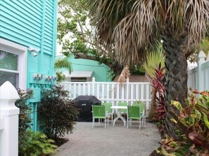 A turquoise house with a white fence, a patio with green chairs and a table, and a grill. - Coco's Island Retreat: Near Gulf, Bay, Bridge St by Anna Maria Life Vacation Rentals (Bradenton Beach)