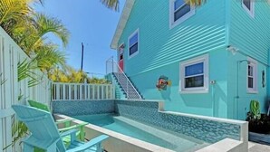 Une maison turquoise avec une petite piscine, une clôture blanche et un escalier menant à la porte.