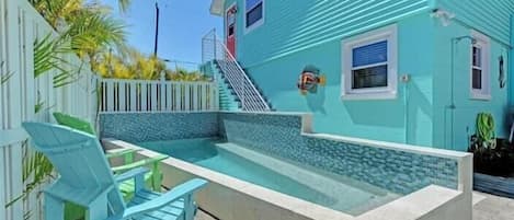 A turquoise house with a small pool, a white fence, and a staircase leading to the door.