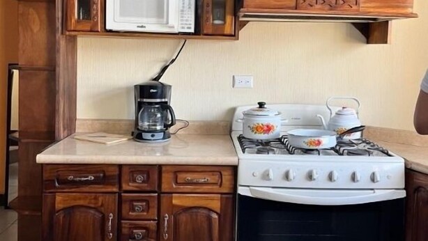 A kitchen with wooden cabinets, a microwave, a coffee maker, and a stove. - Modern and cozy apartment in Quetzaltenango (Quetzaltenango)