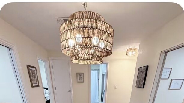 Uma sala de jantar com mesa de madeira, seis cadeiras, um candelabro e quadros decorativos nas paredes.