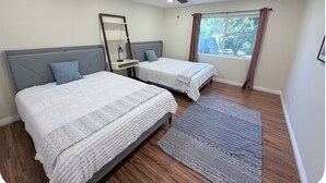 Quarto com duas camas, um ventilador de teto, uma janela com cortinas e uma mesa de cabeceira com abajur.