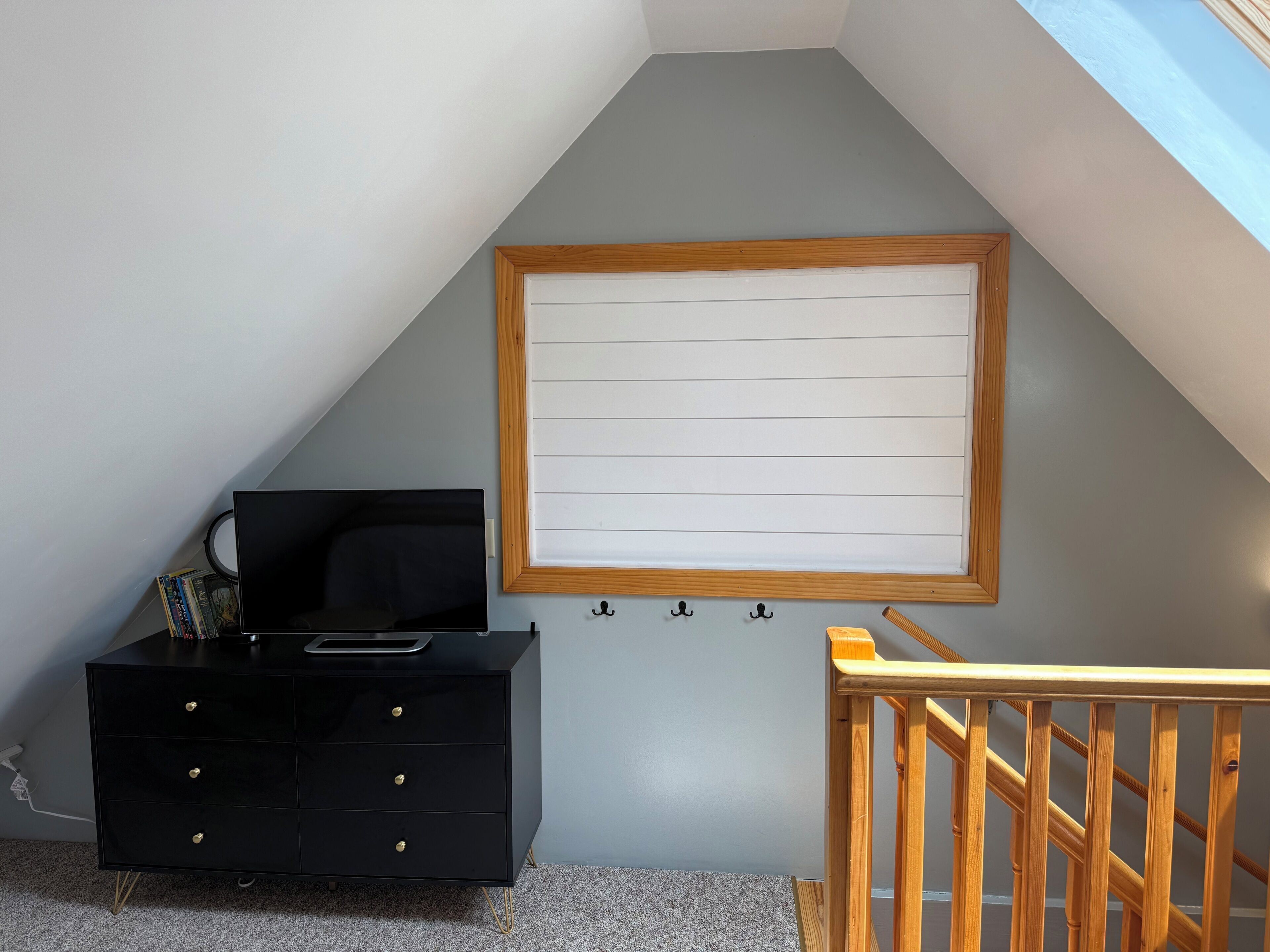 A room with a black dresser, a wooden-framed picture, and a wooden staircase.