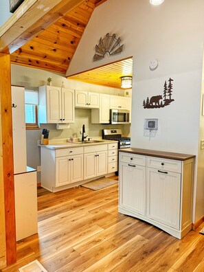 A kitchen with white cabinets, a microwave, and a stove. There is a wooden ceiling and a wall decal of a bear and trees. - Castle Rock Lake Cabin, Sleeps 8, Fire Pit, Secluded, Near WI Dells (Friendship)
