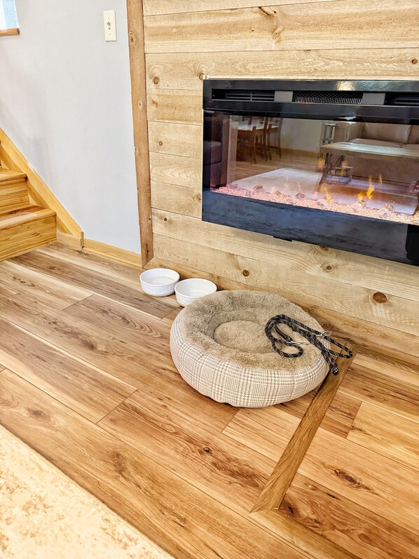 A wooden interior with a fireplace, a pet bed, and bowls on the floor. - Castle Rock Lake Cabin, Sleeps 8, Fire Pit, Secluded, Near WI Dells (Friendship)
