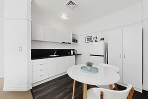 Eine moderne Küche mit weißen Schränken, einer schwarzen Arbeitsplatte, einem runden Tisch mit Stühlen und einer Mikrowelle über der Arbeitsfläche.