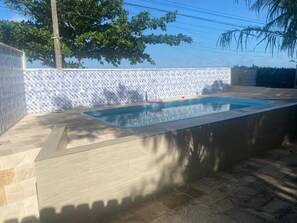Ein rechteckiger Pool mit einer bepflasterten Wand und einer Stein-Terrasse.