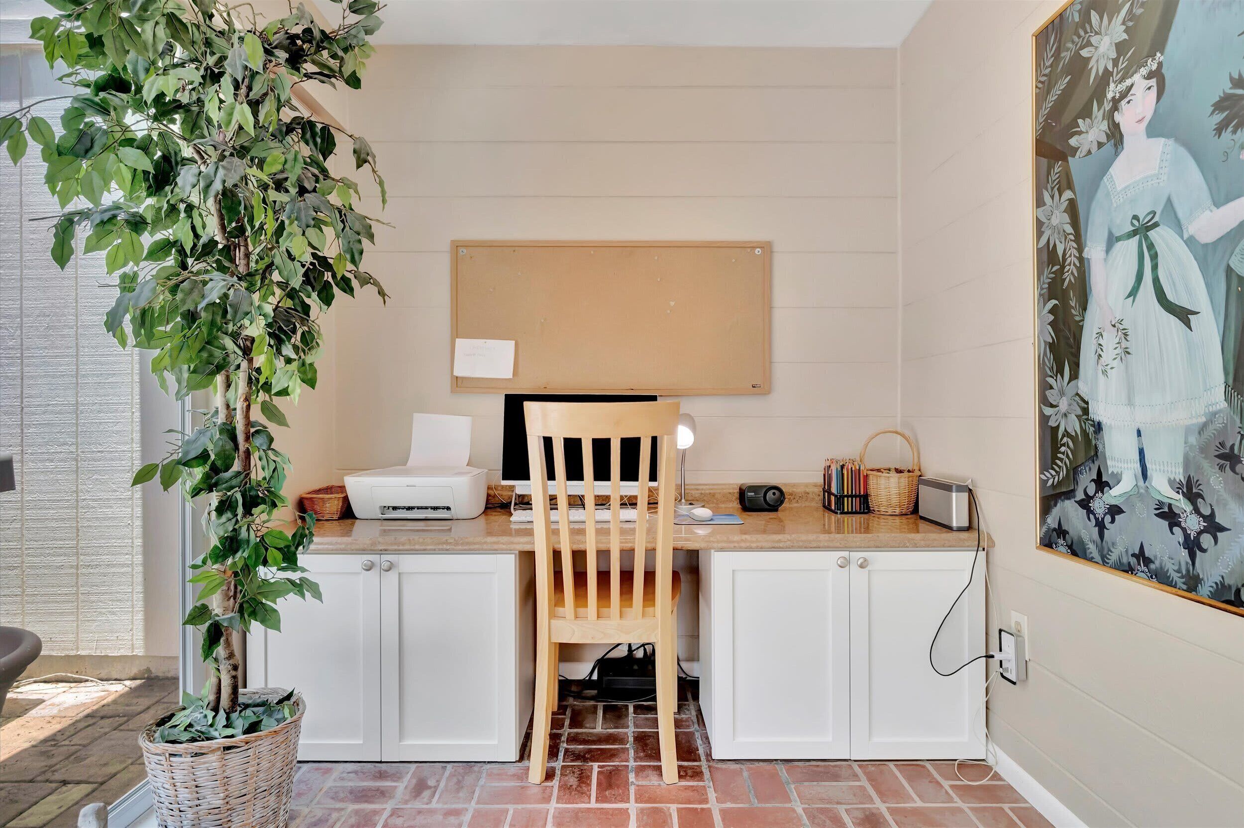 A workspace with a desk, chair, computer, printer, and a potted plant.