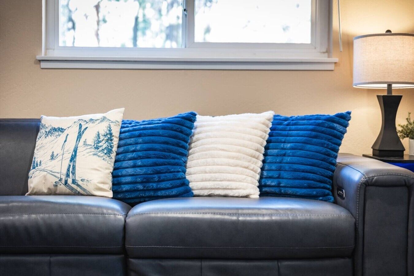 A leather sofa with three cushions in a room with a window and a lamp.