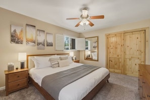 Un dormitorio con cama, mesitas de noche, ventilador de techo, armario de madera y decoración en la pared.