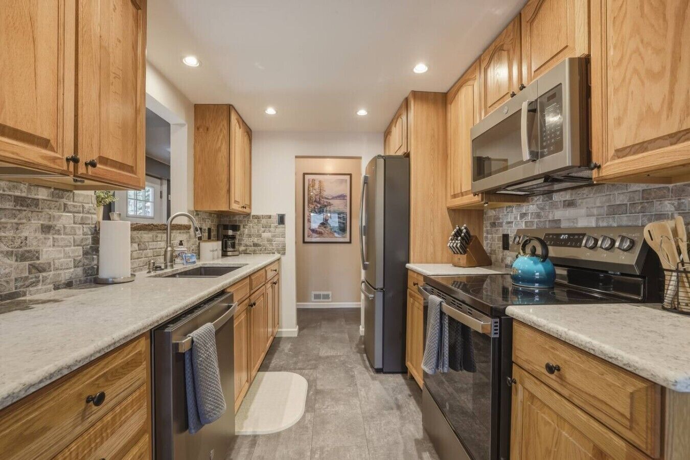 A kitchen with wooden cabinets, a stainless steel refrigerator, a microwave, a stove, and a sink.
