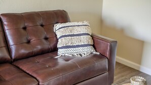 A brown leather sofa with a woven throw pillow.
