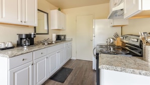 A kitchen with white cabinets, a granite countertop, a coffee maker, a microwave, a stove, and a sink.