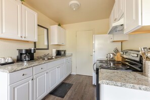 A kitchen with white cabinets, a granite countertop, a coffee maker, a microwave, a stove, and a sink.