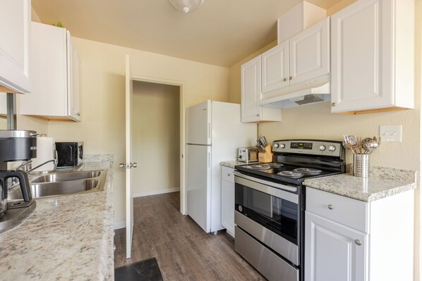 A compact kitchen with white cabinets, a stainless steel sink, a black stove, and a refrigerator. - Cozy 1BR Near Fresno State - WiFi + AC (Fresno)