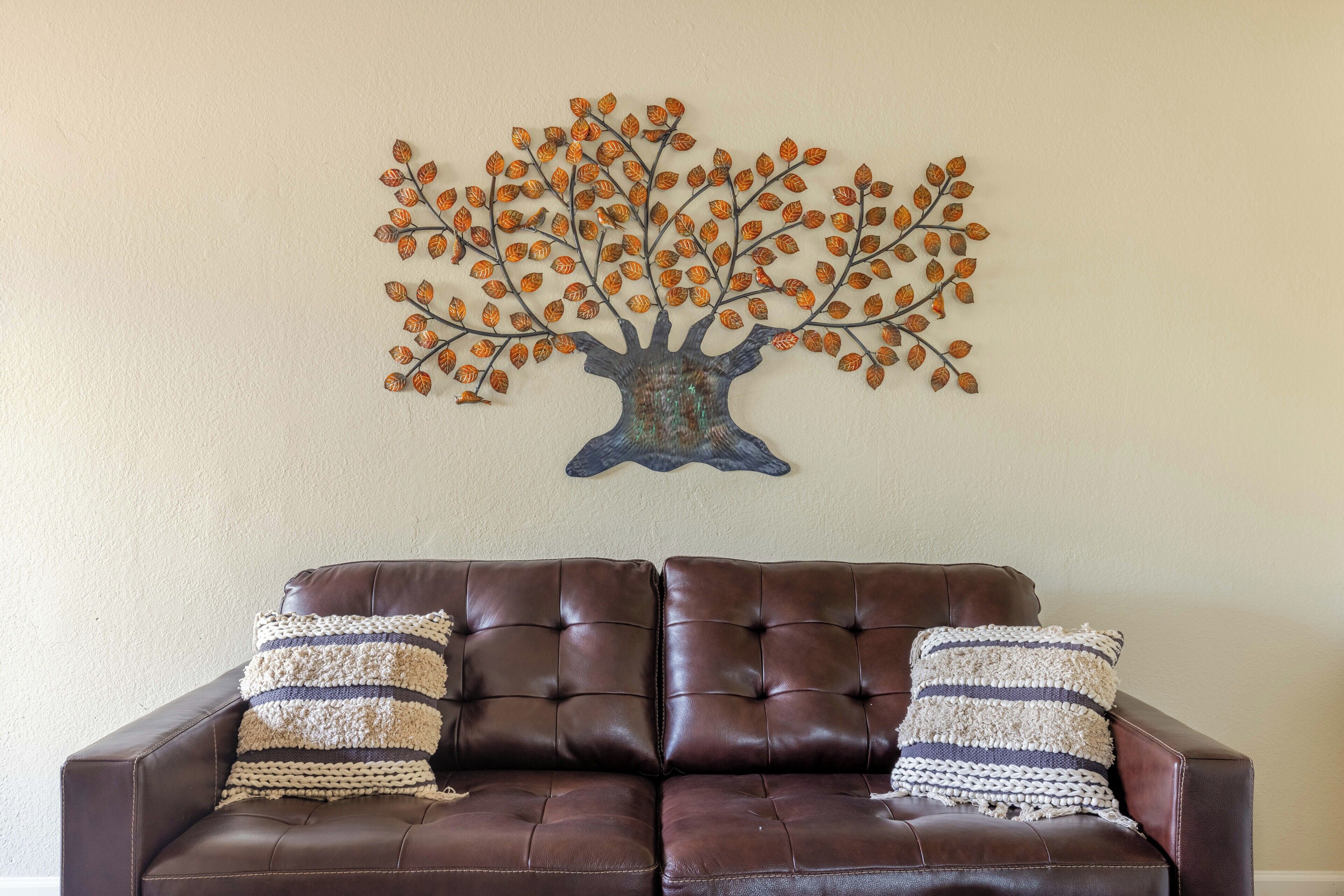 A brown leather sofa with two striped pillows and a wall-mounted tree decoration.