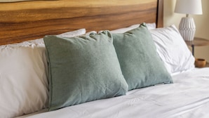 A bed with a wooden headboard, white bedding, and two green pillows.