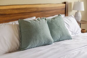 A bed with a wooden headboard, white bedding, and two green pillows.