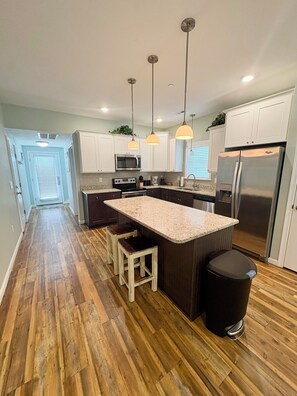 Una cocina moderna con una isla central, taburetes de bar, un refrigerador de acero inoxidable e iluminación colgante.