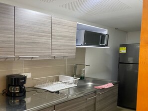 Une cuisine moderne avec des meubles gris, un évier en acier inoxydable, un réfrigérateur noir et un four à micro-ondes.