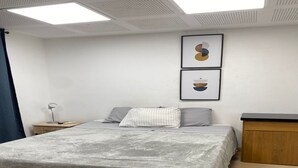 Un dormitorio con cama, mesita de noche, escritorio y dos obras de arte enmarcadas en la pared.