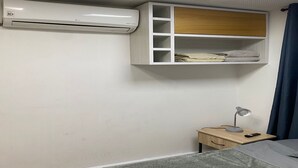Un dormitorio con cama, mesita de noche, escritorio, aire acondicionado y estante empotrado con toallas dobladas.