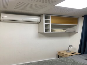 Ein Schlafzimmer mit Bett, Nachttisch, Schreibtisch, Klimaanlage und einem Einbauschrank mit gefalteten Handtüchern.