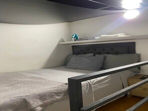 Ein Etagenbett mit Kopfteil, ein Nachttisch mit Fernbedienung und ein oberes Regal.