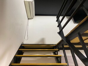 Eine Treppe mit Holzboden und schwarzen Geländern, die zu einem Raum mit weißer Wand und Deckenventilator führt.