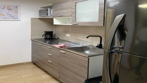 A modern kitchen with a stainless steel refrigerator, wooden cabinets, a coffee maker, and a glass dish rack. - Global Executive Suites 203 (Medellín)