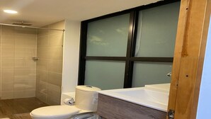 A bathroom with a toilet, shower, and a large window. - Global Executive Suites 203 (Medellín)