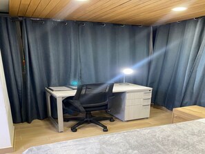 Ein Zimmer mit Schreibtisch, Stuhl und einem kleinen Schrank.