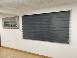 Ein Zimmer mit einem großen, dunkel gefärbten Rollo, einem kleinen Spiegel und einem Holzboden.