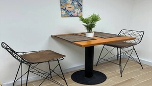 Un pequeño comedor con una mesa de madera, dos sillas de estructura metálica, una planta en maceta y una obra de arte floral en la pared.