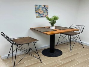 Ein kleiner Essbereich mit einem Holztisch, zwei Gestellstühlen, einer Topfpflanze und einem Blumenbild an der Wand.