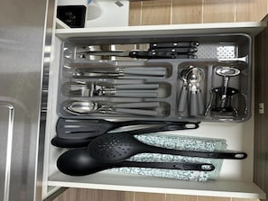 Eine Schublade mit Küchenutensilien, darunter Pfannenwender, Zangen, ein Schöpflöffel und ein Dosenöffner.