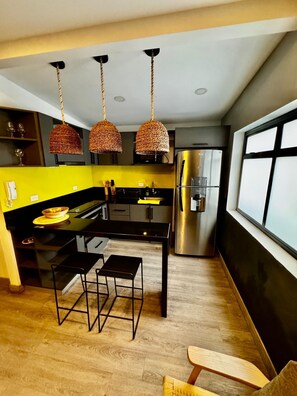 Eine moderne Küche mit einer zentralen Kochinsel, schwarzen Barhocker, einem Edelstahl-Kühlschrank und einem großen Fenster.