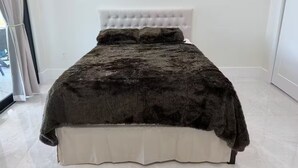 Ein Bett mit einer gepolsterten Kopflehne, einer dunklen Decke und einem weißen Gestell.