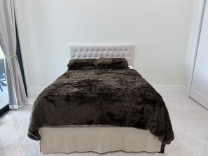 A bed with a tufted headboard, a dark blanket, and a white base. - Naples Vacation Paradise -  Lake & Pool Views (Naples)