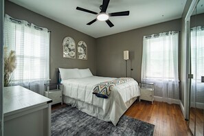 Ein Schlafzimmer mit Bett, Nachttischen, Deckenventilator und einem Fenster mit Vorhängen.