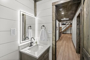 A modern bathroom with a large mirror, a sink, and a wooden staircase leading to another room.