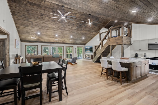 Una cocina amplia con techo de madera, comedor con una mesa grande y sillas, y barra con taburetes.