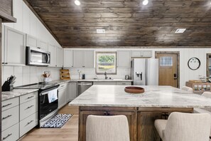 Una cocina moderna con armarios blancos, techo de madera y una isla grande con asientos.