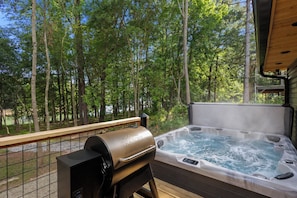 Un jacuzzi con una parrilla en el exterior, rodeado de árboles.