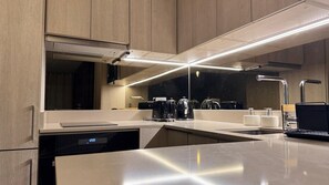 Eine moderne Küche mit einer Edelstahl-Arbeitsplatte, einem integrierten Geschirrspüler, einer Kaffeemaschine und einem Wasserkocher.