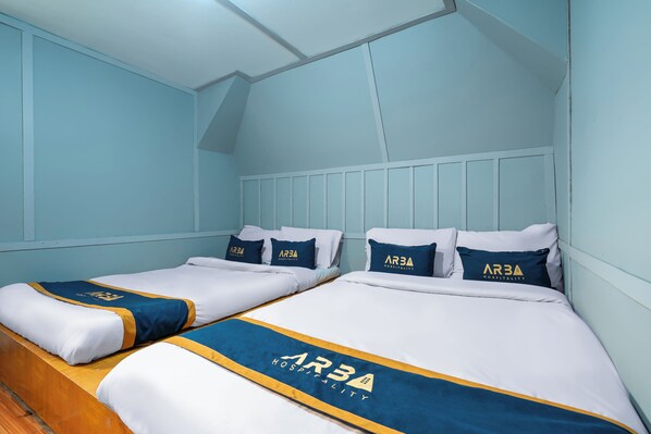 A hotel room with two beds, each with matching pillows and a blue and white bedspread featuring the hotel's logo. - The Cabin Artana (Pangalengan)
